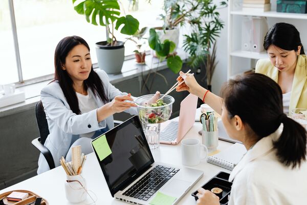 Tres compañeras compartiendo una ensalada en la oficina junto a sus ordenadores.