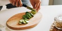 Preparación de alimentos: manos cortando un pepino en rodajas sobre una tabla de madera.